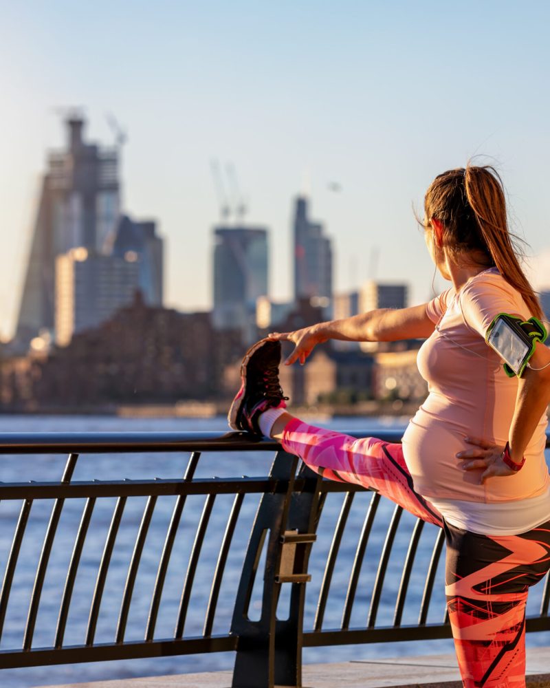 Pregnant woman does her stretching after workout in front of the skyline of London