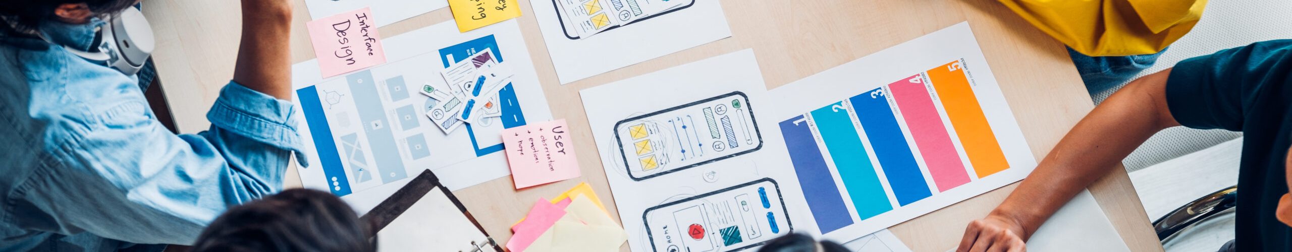top view asian ux developer and ui designer brainstorming about mobile app interface wireframe design on table with customer brief and color code at modern office.Creative digital development agency